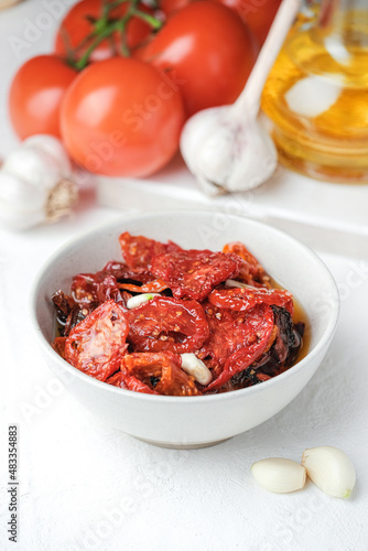 Sun dried tomatoes  on white bowl, white wooden background. Dried tomatoes with olive oil, salt, herbs and garlic recipe.  Top view,  copyspace.