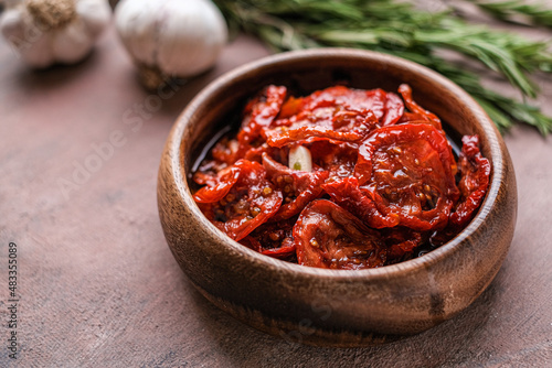 Sun dried tomatoes in wooden bowl. Dried tomatoes with olive oil, rosemary, salt, herbs and garlic recipe. Dark background. 