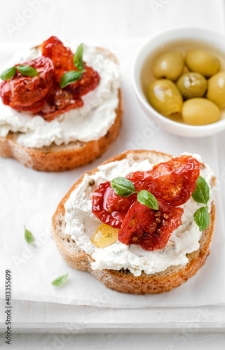 Two bruschettas with ricotta cheese, olive and dried tomatoes on ciabatta bread on white background. Olive oil and spices decorated. Copyspace.