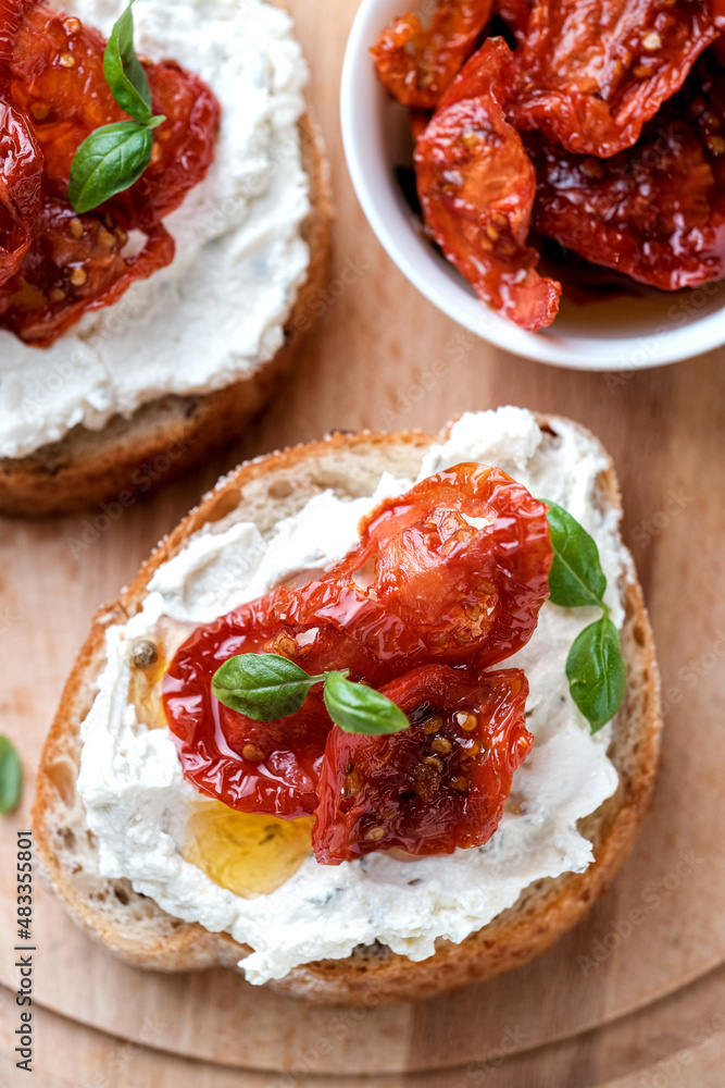 Two bruschettas with ricotta cheese, olive and dried tomatoes on ciabatta bread on white background. Olive oil and spices decorated. Copyspace.