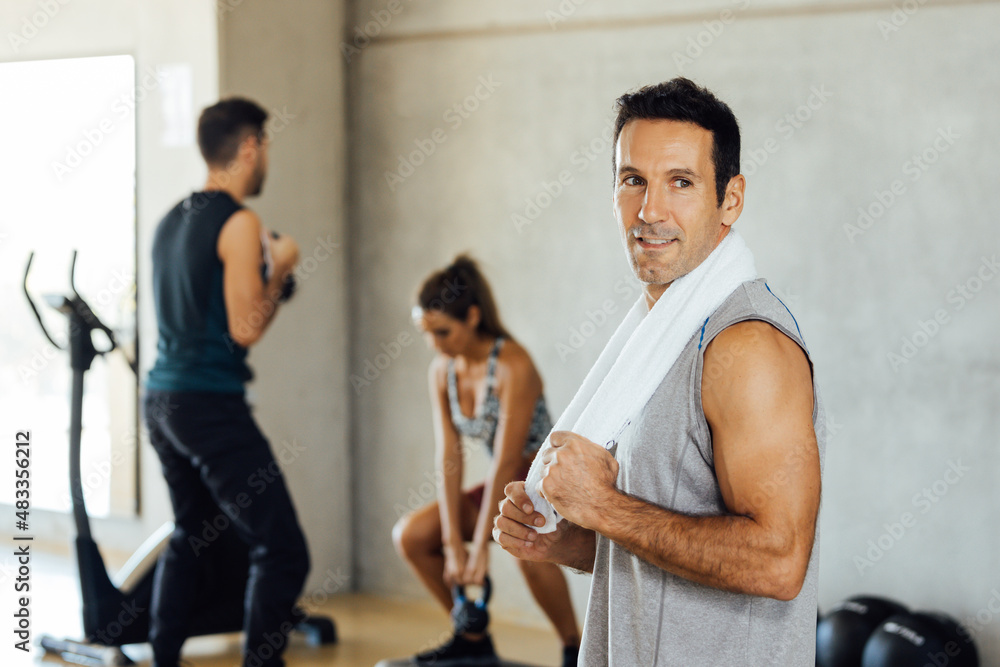 Smiling attractive sporty fit man stands and poses in a gym looking one side. Smiling attractive sporty fit man stands and poses in a gym looking one side.