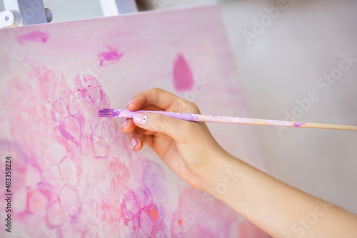 Female artist's hand with brush painting on easel