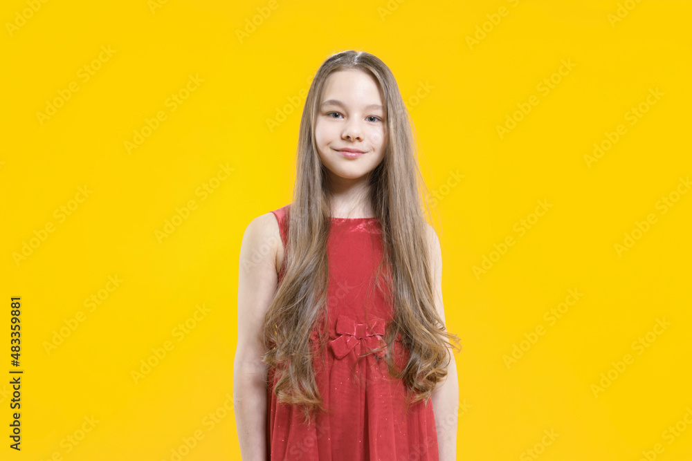 A cute teenage girl in a red dress with long blond hair stands on a yellow background smiling. Pupil. A cute teenage girl in a red dress with long blond hair stands on a yellow background smiling. Pupil.