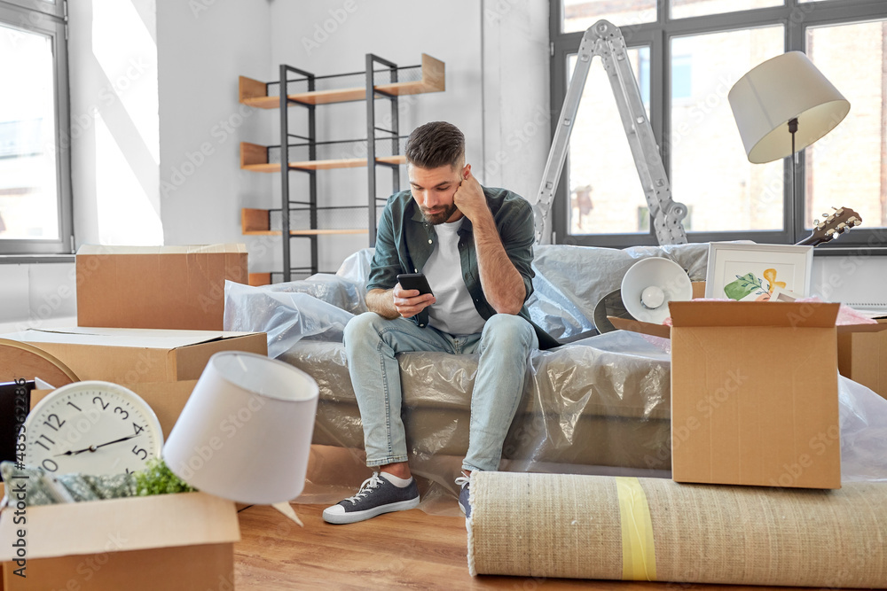 moving, eviction and real estate concept - sad man with smartphone and boxes at new home moving, eviction and real estate concept - sad man with smartphone and boxes at new home