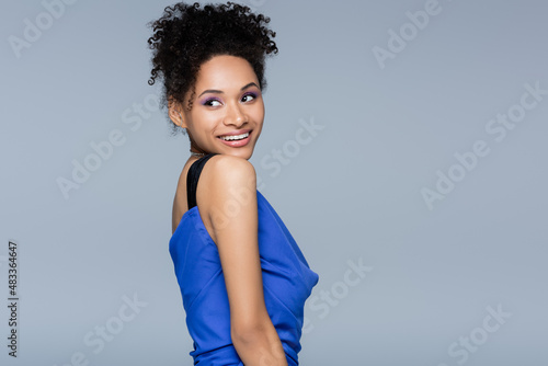 joyful african american woman in bright slip dress looking away while posing isolated on grey.