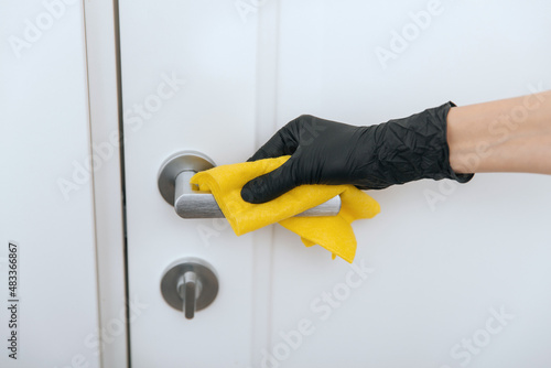 Cleaning door handle with yellow wipe in black gloves. Woman hand using towel for cleaning. Disinfection in hospital and public spaces against corona virus.