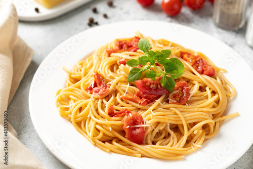Spaghetti with tomatoes, parmesan and basil in a white plate on a bright kitchen table. Traditional Italian pasta with vegetables and cheese 