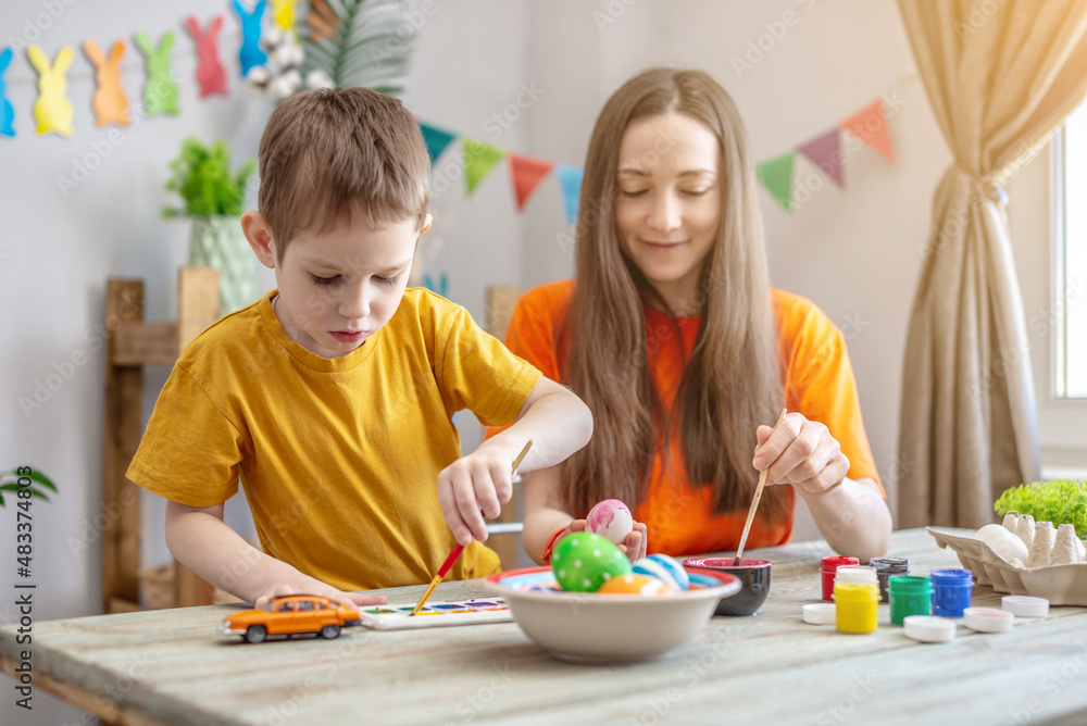 Fototapeta premium Mom and little child together are coloring eggs and having fun. Concept of family preparation for Easter, festive spring mood