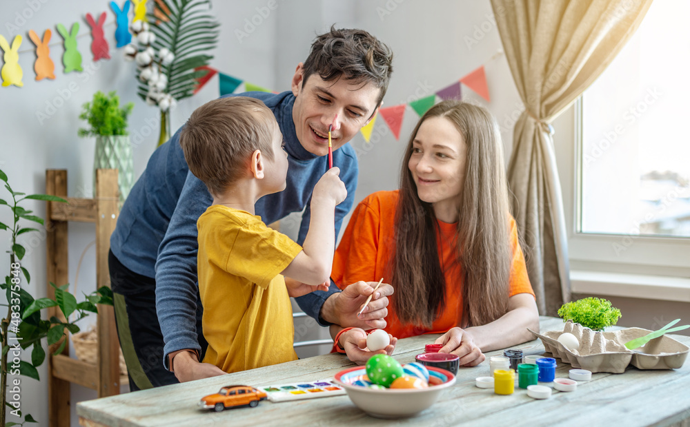 Fototapeta premium Mom, dad and child together are coloring eggs and having fun in a decorated room. Concept of family preparation for Easter, festive spring mood