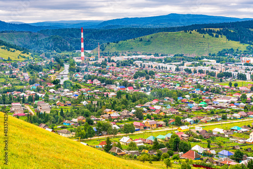 Panoramic view from hill to plain with small town in summer cloudy day. Picturesque urban landscape with many colorful houses. Sim, Chelyabinsk region, Russia. Travel blog concept photo