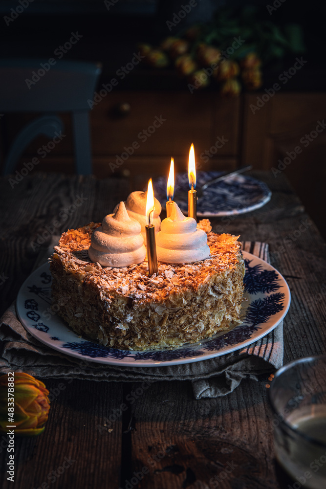 Mille-feuille cake decorated with meringues and three lit candles on vintage plate on old wooden table. Mille-feuille cake decorated with meringues and three lit candles on vintage plate on old wooden table.