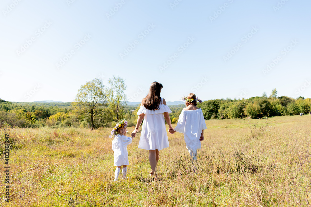 Maternal care. Mom and her two daughters walk around the field holding hands.