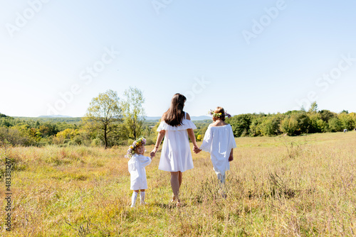 Maternal care. Mom and her two daughters walk around the field holding hands.