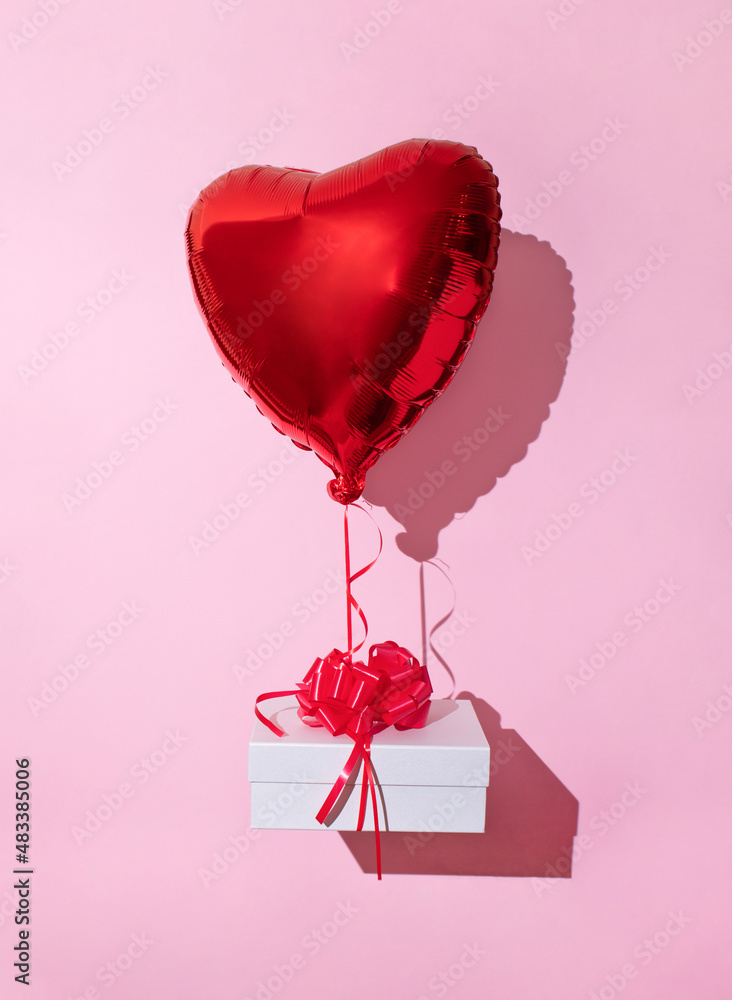 Romantic background for Valentine's Day and birthday. Bright red heart-shaped balloon and white box on a pastel pink background. Holiday and love light minimal layout.