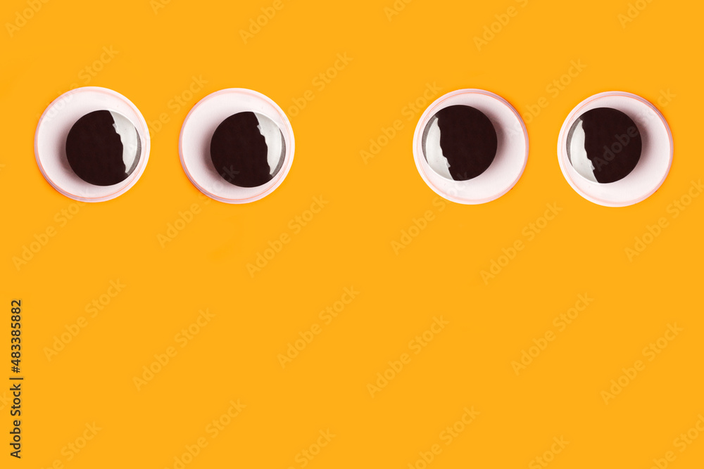 Fototapeta premium Dos pares de ojos grandes de juguete saltones mirandose entre si sobre un fondo anaranjado liso y aislado. Vista de frente y de cerca. Copy space
