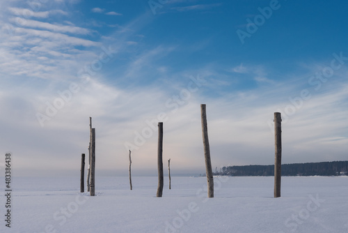 Minimalistic winter landscape. Background. Single wooden poles stand in the middle of a snowy field. The horizon line is visible.