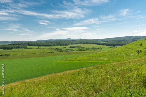 Green valley under blue sky with hills  forest and field. Beautiful landscape as a background