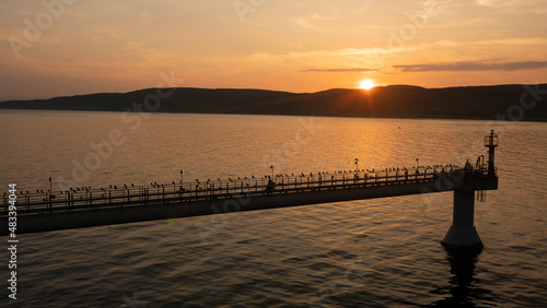 On the coast of the sea  the sun hides behind the mountains at sunset  seagulls fly