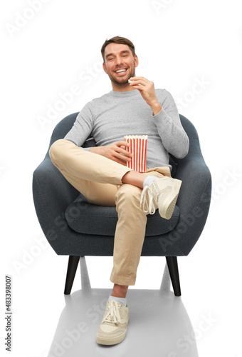 people and leisure concept - happy smiling man eating popcorn sitting in chair over white background