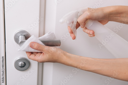 Cleaning white door handles with an antiseptic wet wipe and sanitizer spray. Disinfection in hospital and public spaces against corona virus. Woman hand using towel for cleaning home room door link