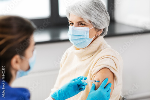 medicine  health and vaccination concept - doctor or nurse with syringe making vaccine or drug injection to senior woman in mask at hospital