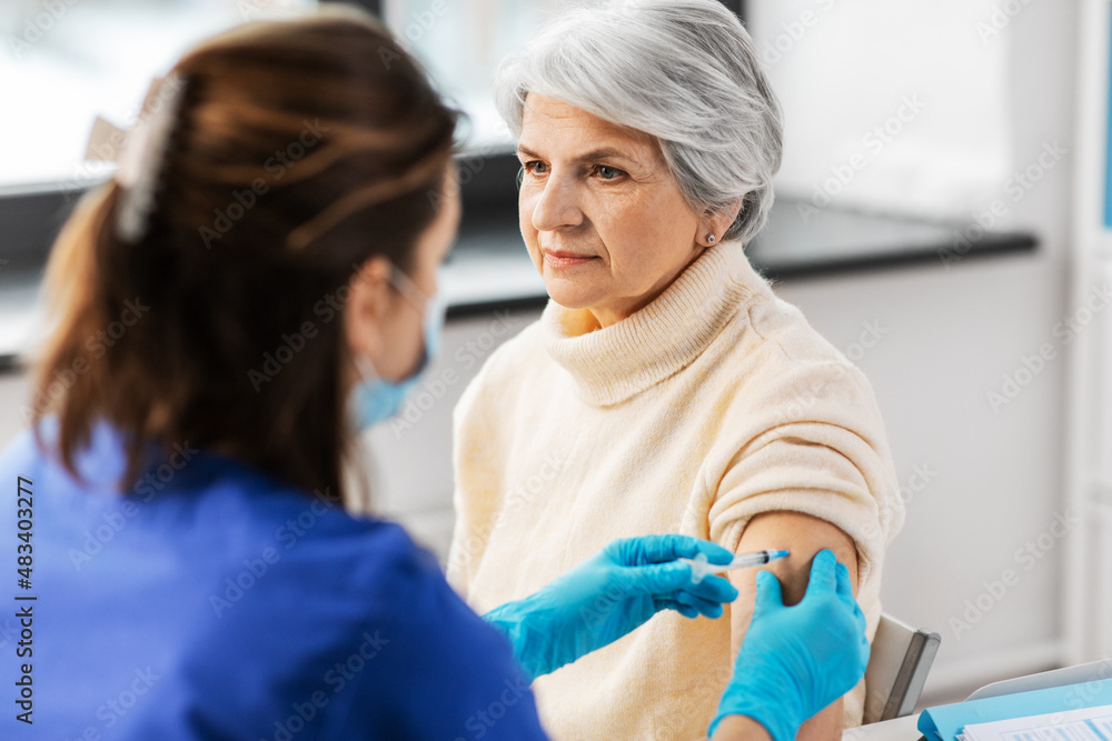 medicine, health and vaccination concept - doctor or nurse with syringe making vaccine or drug injection to senior woman at hospital medicine, health and vaccination concept - doctor or nurse with syringe making vaccine or drug injection to senior woman at hospital