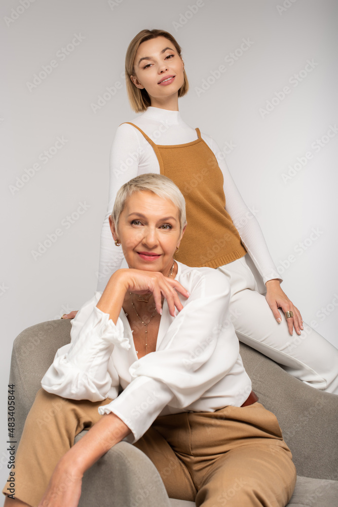 Fototapeta premium joyful young woman near smiling mother sitting in armchair isolated on grey