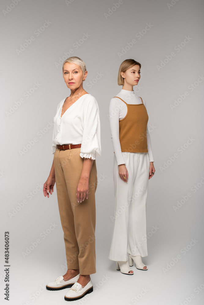 full length of young daughter and stylish middle aged mother standing on grey full length of young daughter and stylish middle aged mother standing on grey