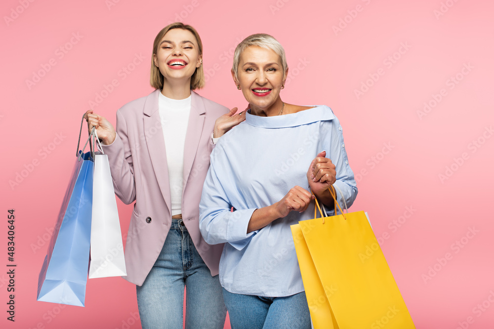 positive young woman and mature mother holding shopping bags isolated on pink positive young woman and mature mother holding shopping bags isolated on pink
