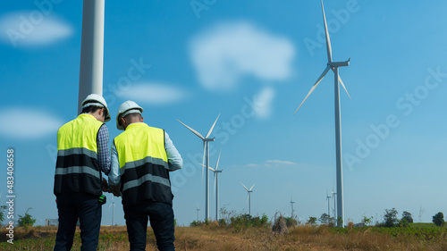 Back view of two engineers discussing against turbines on wind turbine farm.