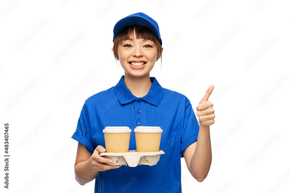 service and job concept - happy smiling delivery woman in blue uniform with takeaway hot drinks in disposable coffee cups showing thumbs up over white background