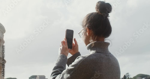 A young woman photographs the Colosseum on a mobile phone photo