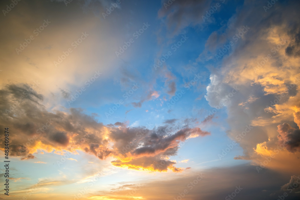 Dramatic sunset landscape picture with puffy clouds lit by orange setting sun and blue sky.