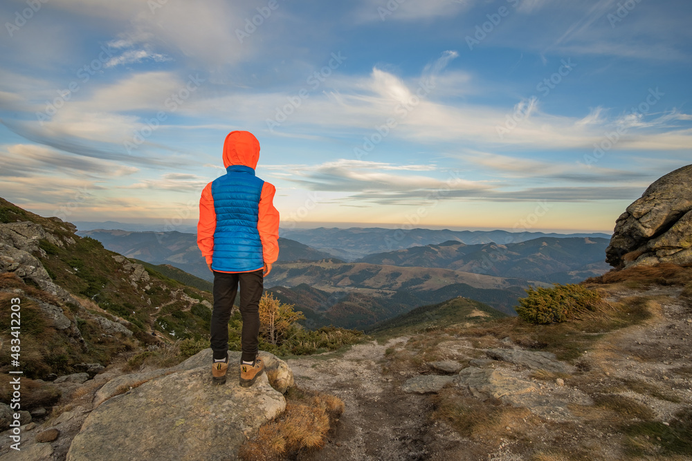 Young child boy hiker standing in mountains enjoying view of amazing mountain landscape.