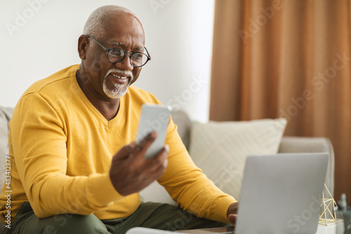 Senior Black Man Using Smartphone And Laptop Working Online Indoors photo