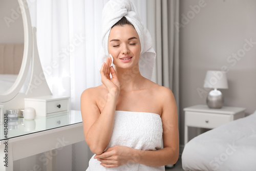 Beautiful young woman with hair wrapped in towel cleaning her face at home