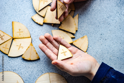 Close-up of a child's hand holding fraction pie chart puzzle pieces
