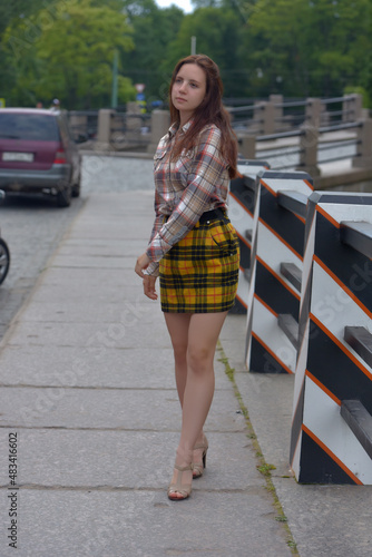 pretty brunette girl in a plaid blouse and skirt on a city street