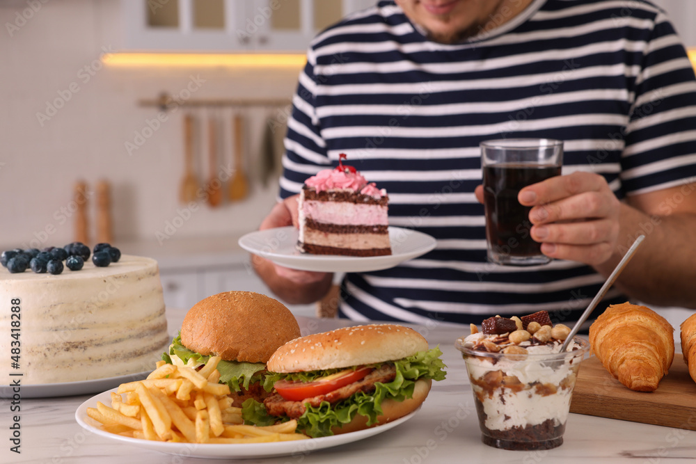 Overweight man with glass of cold drink and cake at table in kitchen, closeup Overweight man with glass of cold drink and cake at table in kitchen, closeup