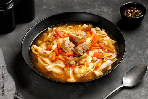 Lagman. The national Uzbek soup with noodles and pieces of meat, fried vegetables. Close up soup. Black plate and black background