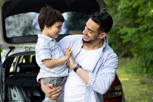 Happy Arab Man With Little Son Standing Near Car With Open Trunk © Prostock-studio