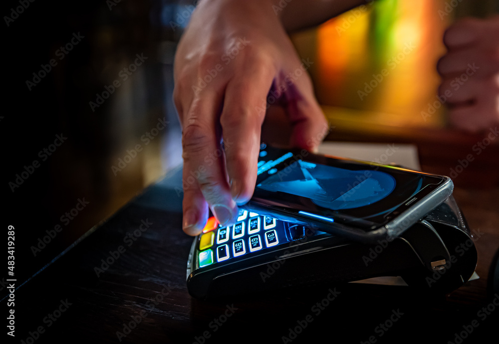 Contactless mobile payment. Payment terminal and smartphone in hands in bar