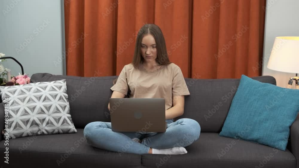 Young woman working on laptop computer, sitting on sofa at home Young woman working on laptop computer, sitting on sofa at home
