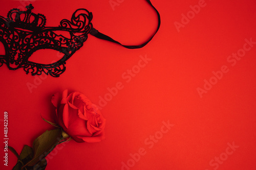 Black mask and red rose on red background. Concept of Valentine's Day, BDSM community. Copy space, top view.
