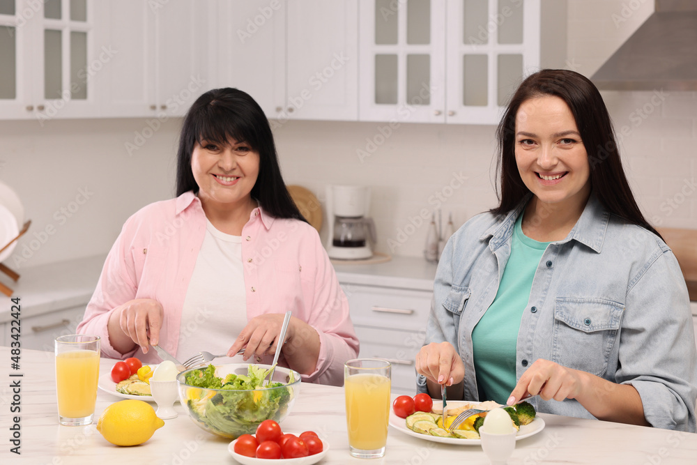 Happy overweight women having healthy meal together at table in kitchen Happy overweight women having healthy meal together at table in kitchen