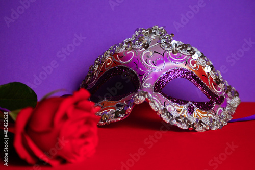 Purple Venetian carnival mask, red rose. Purple-red background .