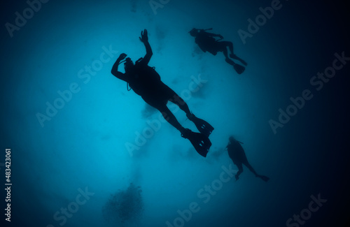 silhouette of three unrecognizable divers in the depths of the sea