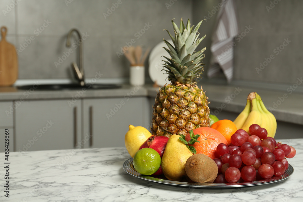 Plate with different ripe fruits on white marble table in kitchen. Space for text