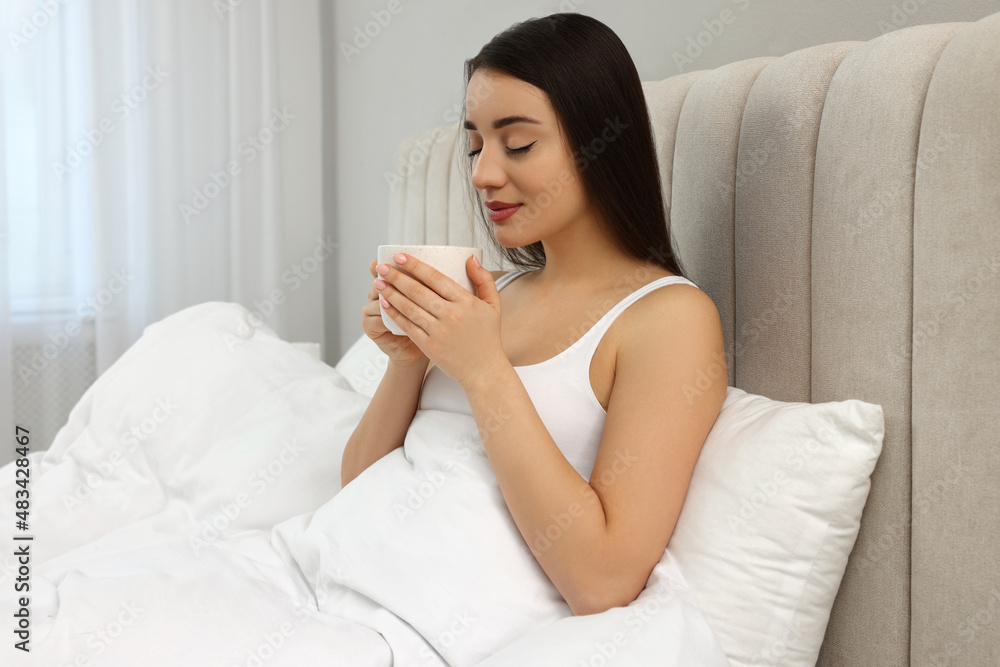 Beautiful young woman with cup of drink in bed at home Beautiful young woman with cup of drink in bed at home