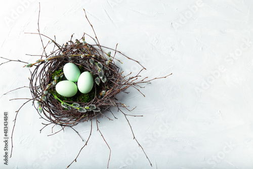 Fotografia Easter Eggs In Natural Nest With Moss And Willow Twigs On White Concrete Background